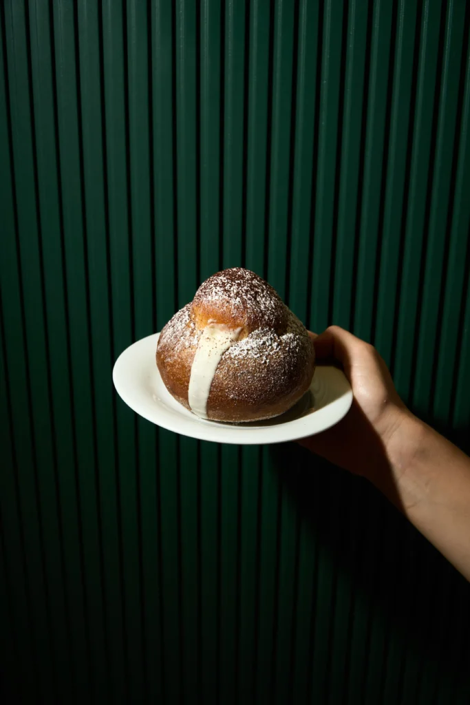 Maritozzo con crema servito su un piattino davanti a una parete verde